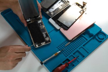 Bir cep telefonu tamircisinin masasında şu anda kullanımda bozulan eskisiyle değiştirmek için cep telefonunun pilini çıkarıyor..