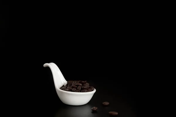 白色陶瓷勺子在黑色背景上充满新鲜咖啡豆 — 图库照片