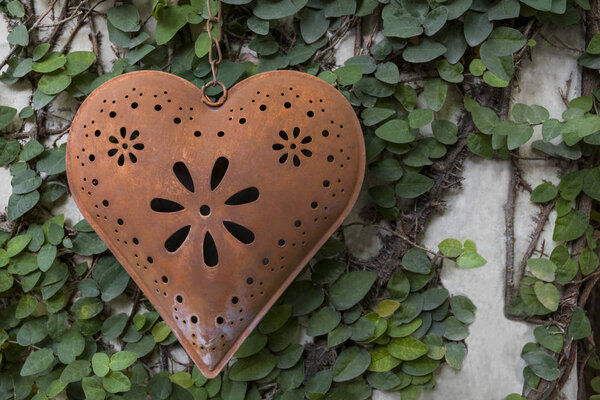 a heart made of beautiful copper metal hangs on green wall
