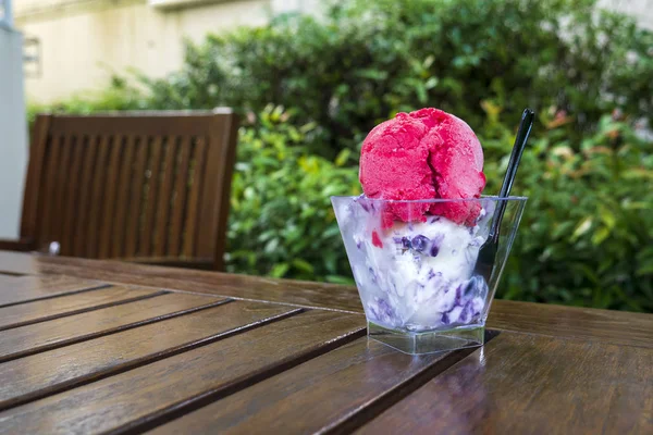 Strawberry ice cream of bright pink in a square plastic cup on a rustic wooden table with a disposable black plastic spoon for refreshing summer snacks. Copy space for your text