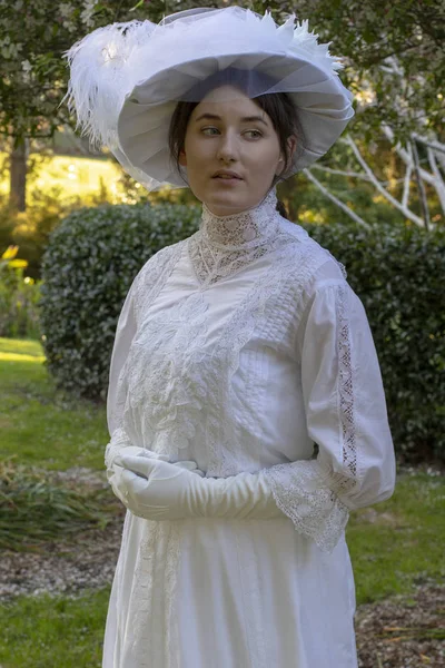 Edwardian woman wearing a white dress and hat in a garden
