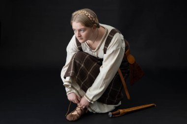 A Viking woman wearing a plaid tunic against a black backdrop clipart