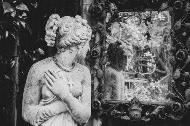 Aşırı büyümüş bir bahçedeki aynaya bakan heykel. Görüntü siyah beyaz