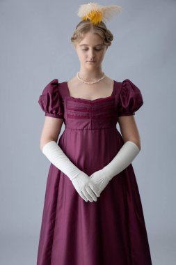 Saçında tüyler olan, erik renkli bir gece elbisesi giyen naip bir kadın.