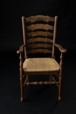 Siyah bir arka planda örülmüş koltuğu olan eski bir ahşap sandalye.