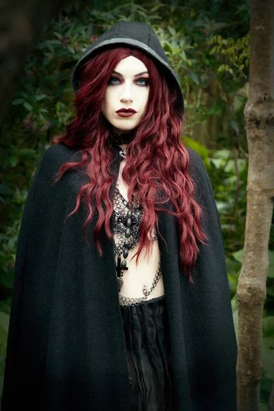 ハロウィンをテーマにしたイメージで森の中に黒いマントを着た女性 — ストック写真