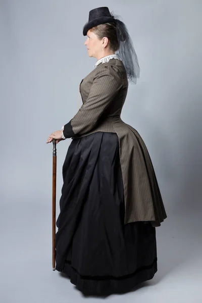 A middle-aged woman in a Victorian costume and holding a silver-topped cane