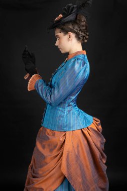 A young Victorian woman in an 1880s ensemble against a black studio backdrop clipart