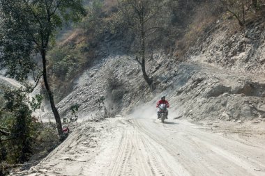 Dağlarda tozlu toprak yol üzerinde sürüş bir motosiklet.