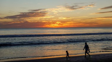 Bazı insanlar gün batımı sırasında sahilde su.