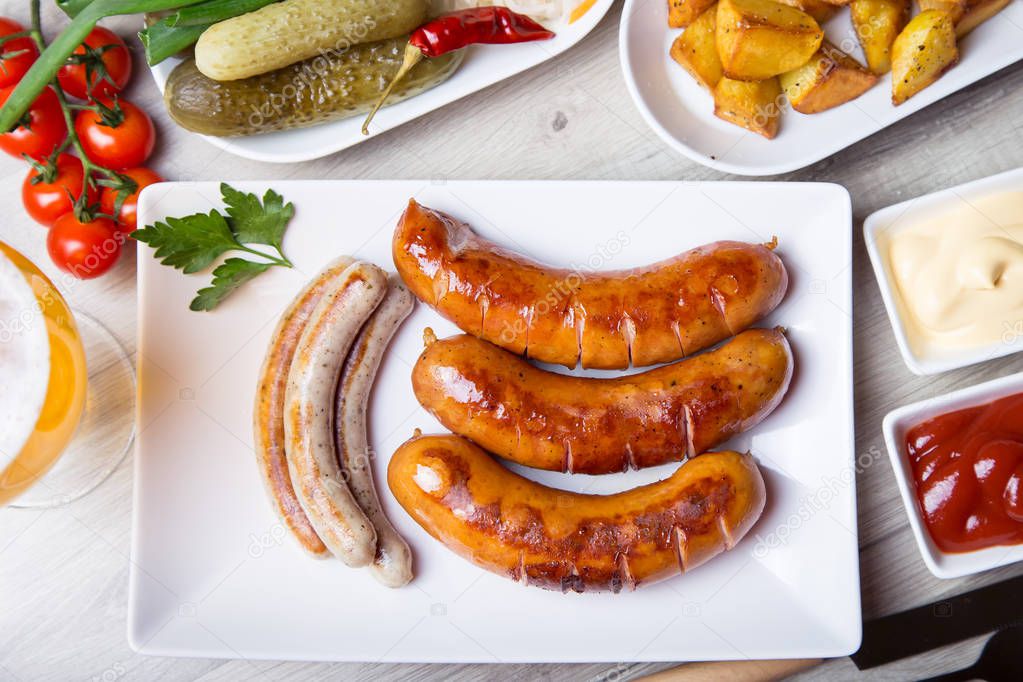 Grilled sausages with potatoes, cucumbers and sauerkraut, with two sauces. Close-up, selective focus.