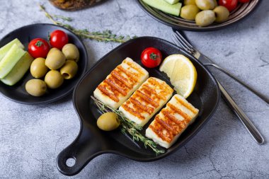 Siyah tavada ızgara haloumi peyniri, zeytin, domates, salatalık ve biberli. Yakın plan..