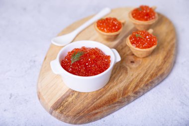 Tahta üzerinde beyaz bir kasede kırmızı havyar (somon havyarı). Arka planda havyarlı tartlar var. Seçici odak, yakın plan.