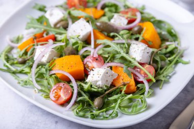 Balkabaklı, peynirli, domatesli, kapari, roka ve kırmızı soğanlı sıcak salata. Yakın plan..