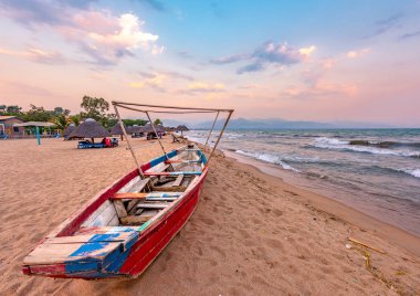 Burundi Bujumbura Tanganika Gölü, rüzgarlı bulutlu gökyüzü ve deniz Gölü içinde ahşap tekne ile Doğu Afrika, Burundi günbatımı kum plaj. Şemsiye Thatch Afrika çatılarda.
