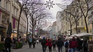 Viyana, Avusturya 17 Aralık 2022 Noel ışıkları altında yürüyen insanlarla dolu alışveriş caddesi ve Advent sezonunda festival süslemeleri. Avrupa kentinde tatil atmosferi ve kış turizmi