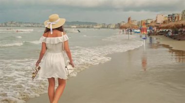 Kumlu sahilde deniz manzaralı çıplak ayakla yürüyen genç bir kadın. 