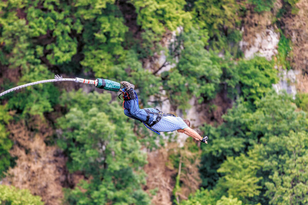 Sochi, Russia - June 7, 2015: Man with go pro camera on wrist jumping 207 meter bungy at AJ Hackett Sky Park on mountain forest background. Extreme activities of Sochi mountain resort