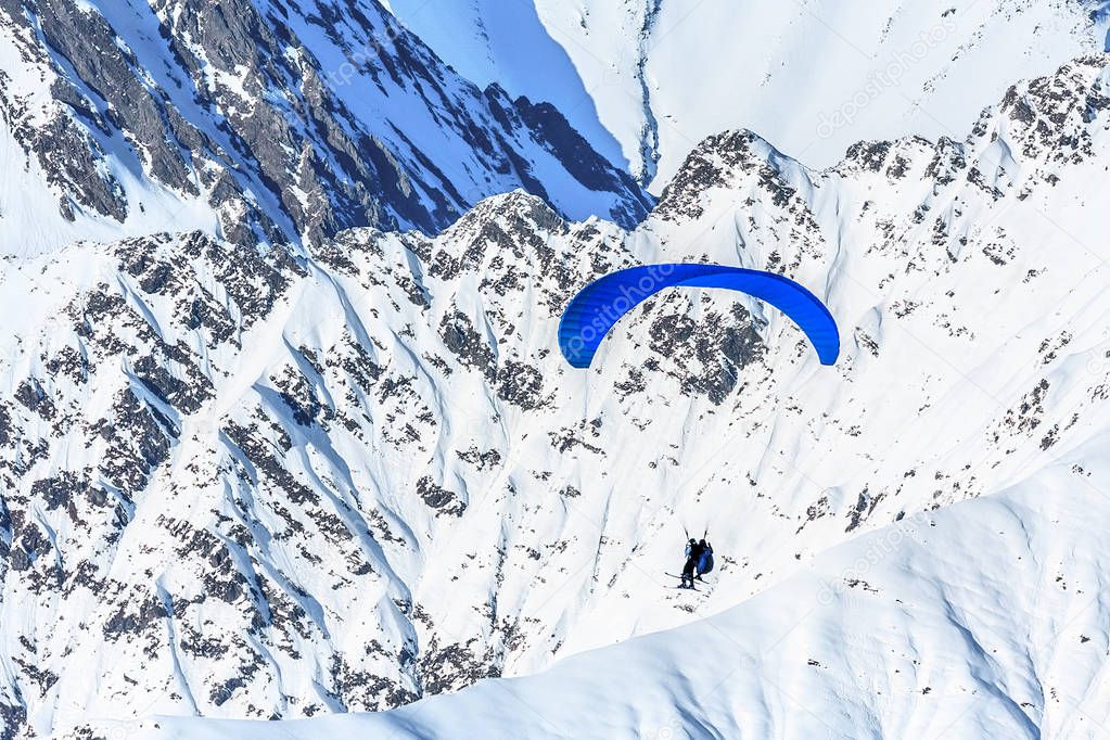 Tandem paragliders soaring against snowy mountain peak. Extreme prarglide winter flight.