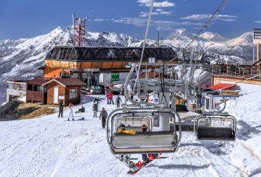 Sochi, Russia - March 25, 2014: Mountain ski slopes of Gorky Gorod ski resort host skiers and snowboarders all winter long. Boarders ride on chair ski lift on snowy peaks and blue sky background