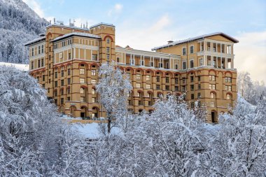 Sochi, Russia - January 9, 2015: Modern and fashionable Novotel Resort Krasnaya Polyana Sochi Hotel is located on snowy mountain slope and surrounded by picturesque winter Caucasus Mountains scenery clipart