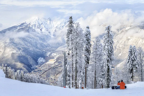 Erkek snowboard oturur karlı kış Dağı'nda Gorki Gorod kayak merkezi, Sochi, Rusya eğimlidir. Kafkas Dağları güzel doğal manzara Krasnaya Polyana Köyü ve kar kaplı