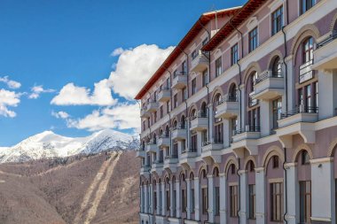 Sochi, Rusya Federasyonu - gerçekleştirilecektir 10, 2014: Modern Rixos Sochi Krasnaya Polyana otel Gorki Gorod dağ kayak resort cephede karlı dağ zirveleri mavi gökyüzü sahne binası. Bahar güneşli doğal manzaraya