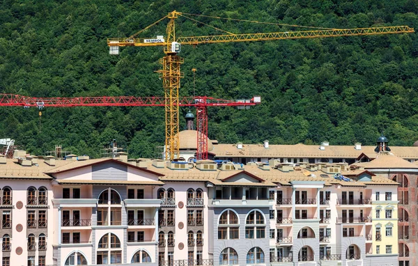 Soçi, Rusya - 12 Ağustos 2013: Gorky Gorod dağ kayak merkezi nin 2014 Olimpiyatları için otel inşaatı. Yaz aylarında yeşil orman arka plan üzerinde binaların üzerinde vinçkule kaldırma