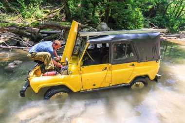 Sochi, Rusya Federasyonu - Haziran 9, 2009: Sarı off-road Rus araba dağ nehirde jeeping sırasında ani arıza sıkışmış. Hood ile belgili tanımlık auto sabitleme sürücü kaldırdı. Doğal güneşli yaz orman görünümünde