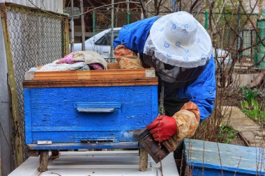 Krasnodar, Rusya - 9 Mart 2009: Arıcı adam koruma maskesi ve diğer iş ekipmanları arı kovanı dezenfekte ve kırsal ev arı kovanı çiftlikte bal toplama