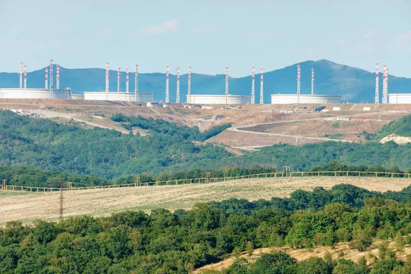 Ηλιόλουστο τοπίο των βουνών του Καυκάσου και των πετρελαιοφόρων και άλλων βιομηχανικών υποδομών της εταιρείας μεταφοράς πετρελαίου-κοινοπραξία αγωγού της Κασπίας στον ορίζοντα — Φωτογραφία Αρχείου