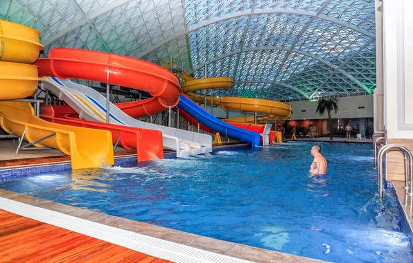 Mountain Beach Water Park in Gorky Gorod resort. Interior view with people bathing in pool by water hills — Stock Photo, Image