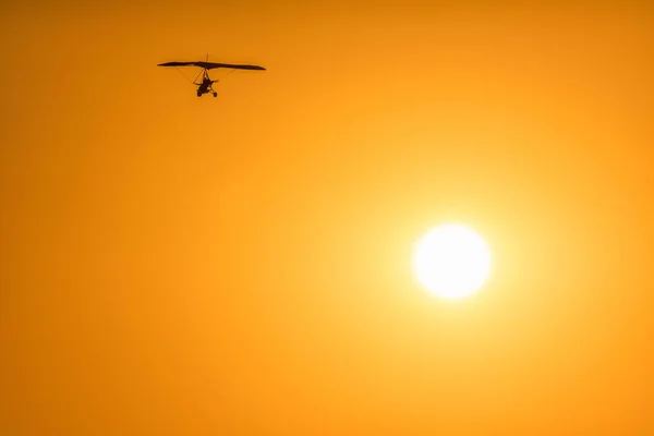 Silhouette of a motor glider flying high in orange sunset sky on sun disc background