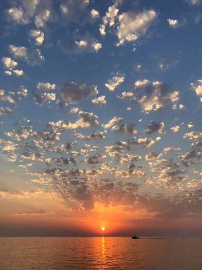 Yayılan güneş ışınları, bulutlar ve sakin deniz suyu ile güzel doğal günbatımı deniz manzarası