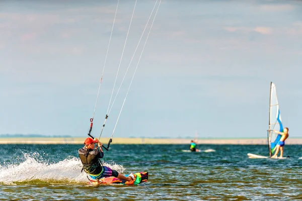 Anapa, Rusia - 9 de julio de 2017: Hombre kitesurfer paseos cometa salpicaduras en la superficie plana de Bugaz firth en el Mar Negro Blaga Beach resort. Destino popular de kitesurf y windsurf. Paisajes soleados de verano — Foto de Stock