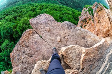 İnsan yürüyüşçü altında yeşil orman ağaçları ile uçurumun üzerinde dağ kayanın kenarında adımlar. Kafkasya dağ yaz manzarası. Lenina Dağı'ndaki Eagles Rock Rafı. Balık gözü görünümü.