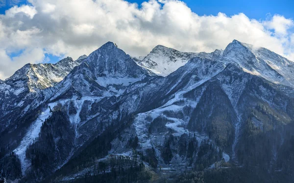 Hermoso paisaje de otoño de picos nevados de Aibga bajo el cielo azul con nubes en las montañas del Cáucaso, pistas de esquí de la estación Gorky Gorod, Krasnaya Polyana, Sochi, Rusia . —  Fotos de Stock