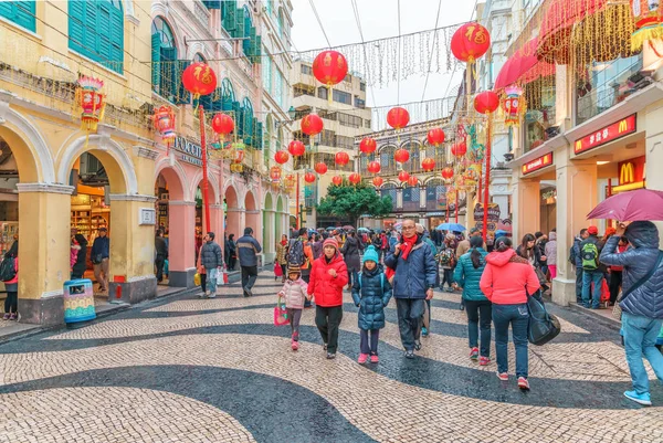 Macao, Çin - 24 Ocak 2016: Senado Meydanı sokak Çin Yeni Yılı kutlamaları kırmızı Çin fener çelenk ile dekore edilmiştir. İnsanlar ellerinde şemsiyelerle şenlikli cadde boyunca yürüyorlar. Makao şehir manzarası. — Stok fotoğraf