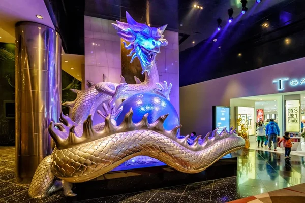 Macao - 24 gennaio 2016: Grande scultura illuminata di drago cinese colorato che tiene la perla negli artigli nel resort City of Dreams Macau. Vista interna con le persone . — Foto Stock