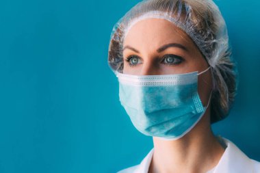 Tıbbi başlık takmış genç bir kadın doktor portresi ve mavi arka planda beyaz önlük ve yazı için yeri var. Klinikteki kadın doktor, Coronavirüs salgını sonrası yorgun doktor.