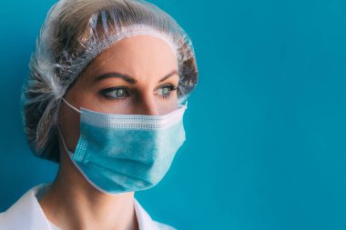 Tıbbi başlık takmış genç bir kadın doktor portresi ve mavi arka planda beyaz önlük ve yazı için yeri var. Klinikteki kadın doktor, Coronavirüs salgını sonrası yorgun doktor.
