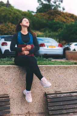 Yeşil arka planda not defteri ve kalemle parkta genç bir kadın. Dilek Maratonu. Bir deftere hayaller ve dilekler yazıyorum. Temiz bir sayfa açarak. Yeni bir hafta planlıyorum. Karantina salgınından sonraki yaşam