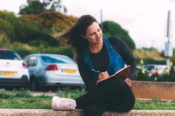 Young woman in park with notebook and pen on green background. Wish Marathon. Writing dreams and wishes in a notebook. Life with a clean slate. Planning a new week. Life after quarantine epidemic