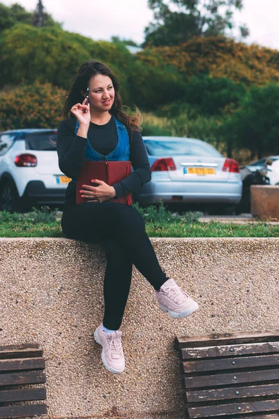 Yeşil arka planda not defteri ve kalemle parkta genç bir kadın. Dilek Maratonu. Bir deftere hayaller ve dilekler yazıyorum. Temiz bir sayfa açarak. Yeni bir hafta planlıyorum. Karantina salgınından sonraki yaşam
