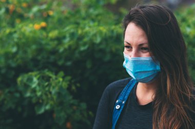Yüzünde koruyucu tıbbi maske takan ve dışarıdaki kameraya bakan genç bir kadının yakın plan portresi. Cerrahi maskeli güzel bir esmer. Karantina sonrası yaşam, koronavirüs salgını