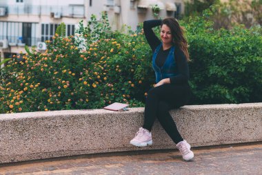 Parktaki genç kadın taş bir bankta oturuyor, bir defter ve tıbbi maskenin yanında. Koronavirüs enfeksiyonu karantinasından sonra dolu dolu bir hayat. Temiz bir sayfa açarak. Virüse karşı zafer. Yeni gerçeklik