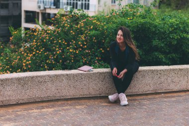 Parktaki genç kadın taş bir bankta oturuyor, bir defter ve tıbbi maskenin yanında. Koronavirüs enfeksiyonu karantinasından sonra dolu dolu bir hayat. Temiz bir sayfa açarak. Virüse karşı zafer. Yeni gerçeklik