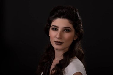 Siyah arka planda beyaz elbiseli okçu bir kadının yakın plan portresi. Yunan tanrıçası Artemis. Stüdyo fotoğraf çekimi. Uzun siyah saçlı bir esmer için profesyonel makyaj ve saç stili. Genç kadın.