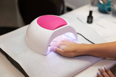Masadaki çiviler için güzel kadın elleri ve lamba. Tırnak jölesi salonu. UV lambası. Çivilerin üzerindeki kurutma jölesi. Güzellik ve kendine dikkat. Manikür salonundaki modern teknoloji. Karantina sonrası çivi bakımı