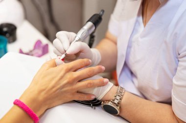 Kuaförde yakın çekim donanım manikürü. Eski jel verniğinin çıkarılması. Manikür ustası müşteri için güzellik prosedürü uyguluyor. Karantinadan sonra çivi bakımı. Beyaz eldivenli bir manikürcünün kadın elleri.